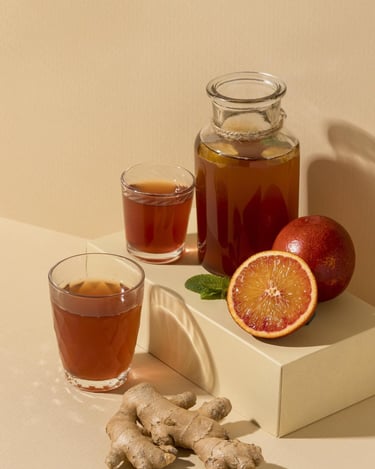 Té de kombucha en una jarra de vidrio, servido con rodajas de naranja  y raíz de jengibre cruda.
