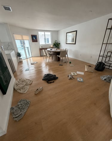 Messy modern living room with items scattered on light wood floors near a round dining table.
