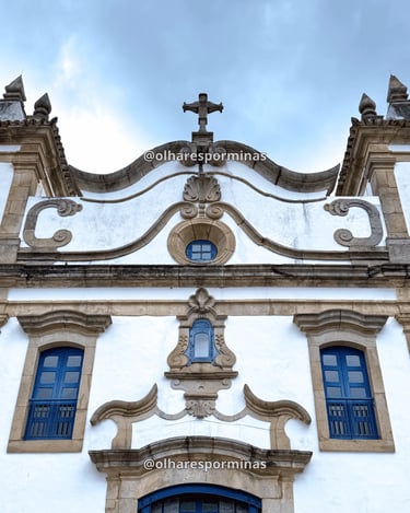 Detalhes da fachada barroca da igreja de Glaura MG com janelas azuis e cruz