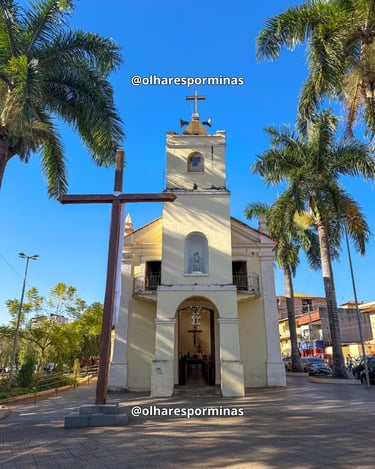 Fachada da Igreja Matriz de Itatiaiuçu com cruz de madeira e palmeiras sob o céu azul