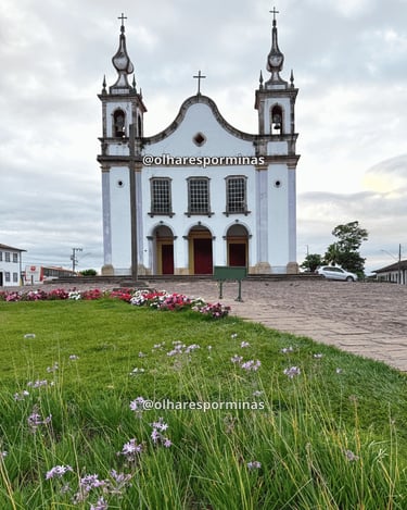 Igreja histórica em Catas Altas MG com jardim florido, torres coloniais e céu nublado ao fundo