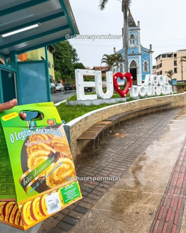 Rocambole tradicional de Lagoa Dourada com letreiro turístico e igreja ao fundo em Minas Gerais