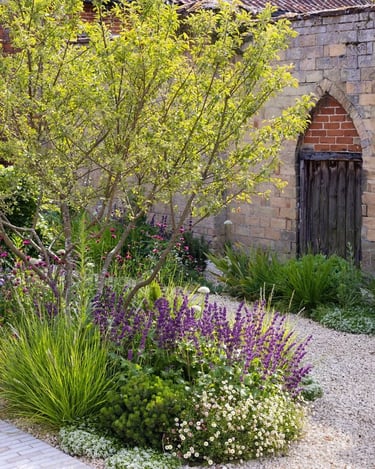 Layered garden planting with flowering perennials, shrubs and a brick wall, creating a natural outdo