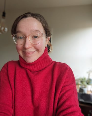 A portrait photograph of female facilitator wearing a red roll neck jumper and glasses