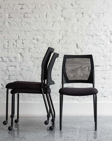 Stacked and upright V137 chairs against a white brick wall, front and side view
