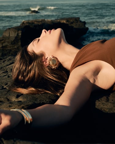 Portrait of Anna lying on a volcanic cliff by the sea, her eyes closed, head tilted toward the sunlight.