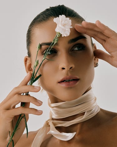 Close-up portrait of Katya holding a flower near her face, wearing a wrapped neck scarf in studio light.