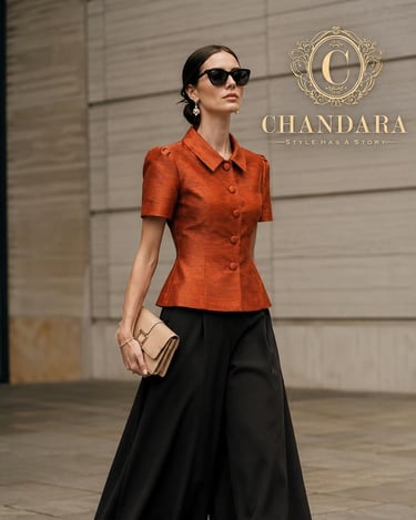 Elegant woman in a burnt orange peplum blouse and black wide-leg trousers by Chandara.