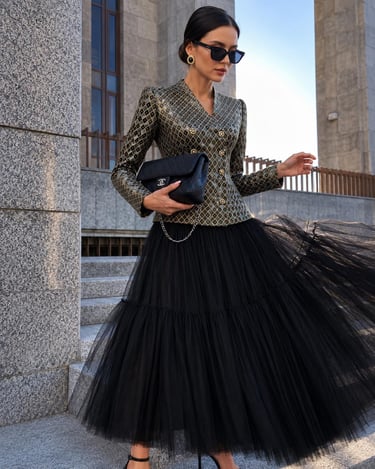 Woman wearing a metallic checkered blazer and black tulle skirt while holding a designer handbag.