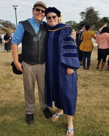 Dr. Laura Hooton, right, in Ph.D. graduation robes with husband at outdoor graduation, Santa Barbara