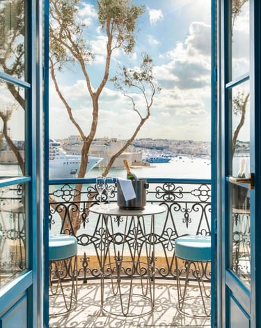 Luxury balcony view of Valletta harbor in Malta with champagne and blue shutters.