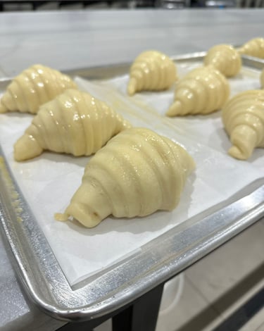 Freshly rolled raw croissant dough resting on a baking sheet with parchment paper in a professional bakery.