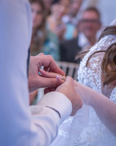 Groom sliding a gold wedding band onto the bride's finger during a marriage ceremony.