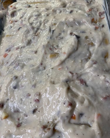 Close-up of creamy white lasagna sauce with vegetables and herbs being spread in a baking dish.