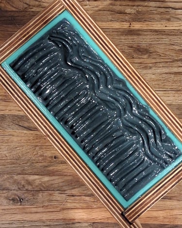 Overhead view of a handmade wooden soap mold filled with swirling charcoal grey artisan soap batter.