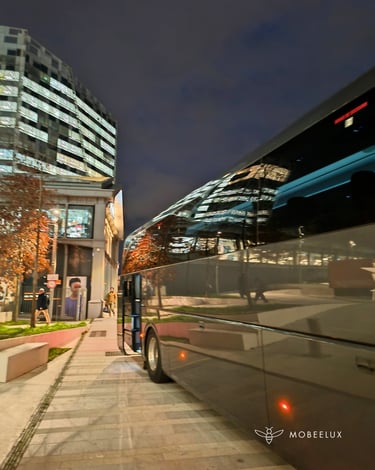 Luxury charter bus parked on a city street at night with reflections of modern office buildings.
