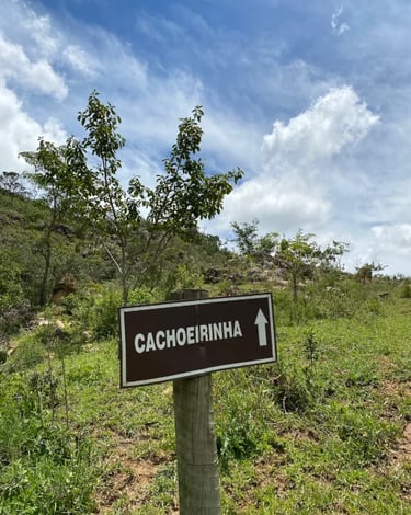 Placa indicando a Cachoeirinha em trilha na Serra da Canastra MG, cercada por vegetação e céu azul