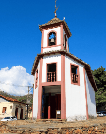 Vista externa da Capela de Nossa Senhora do Ó, com cores vermelho e branco, céu azul em Sabará MG