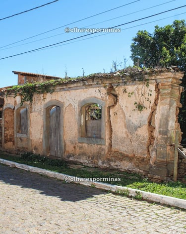 Casarão antigo em Itatiaia, distrito de Ouro Branco MG, com ruínas históricas e rua de pedra sob céu