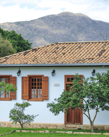 Casa histórica com janelas e porta, telhado bege e montanha ao fundo, em Chapada MG