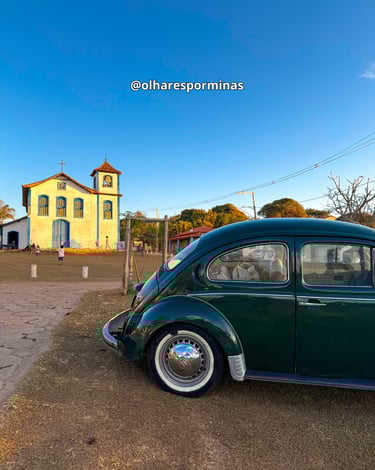 Um fusca de cor verde com a Igreja de Nossa Senhora do Rosário ao fundo em Extração MG