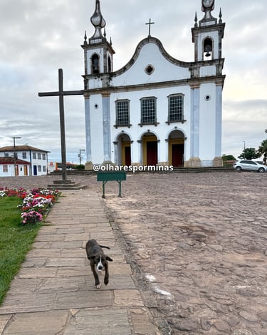 Igreja Matriz de Catas Altas, com uma cruz e um cachorro a frente 