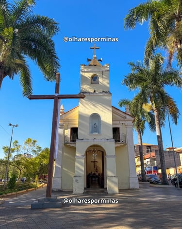 Fachada da Igreja Matriz de Itatiaiuçu com cruz de madeira e palmeiras sob o céu azul