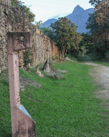 Marco da Estrada Real em frente ao Bicame de pedra com montanha ao fundo e vegetação