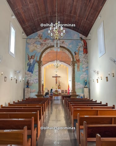 Interior da Igreja Matriz de Itatiaiuçu com bancos de madeira, lustres e pinturas religiosas no alta