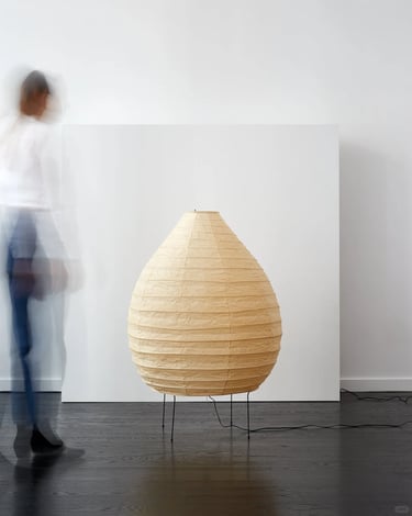 Single Akari paper lamp glowing softly beside a blurred figure, showing the quiet atmosphere of Nogu