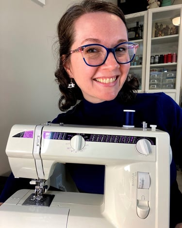 Close-up of a woman with glasses and brown hair smiling behind a sewing machine.