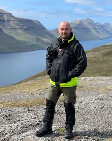Bogi Olsen, your local Faroe Islands photography guide, standing outdoors with camera gear and scenic fjords behind him
