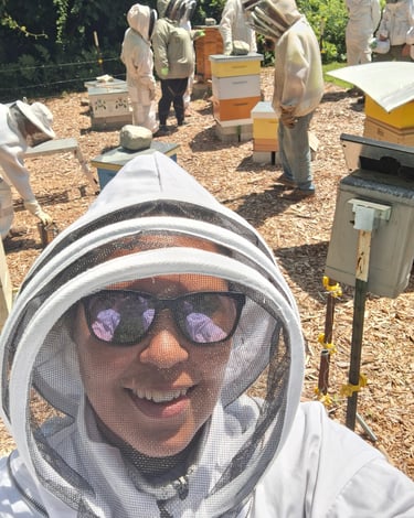 A smiling beekeeper in a protective veil takes a selfie with a group tending to beehives.