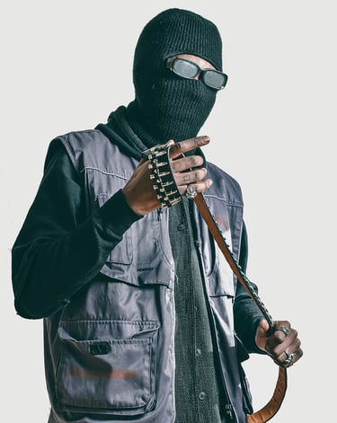 Studio photo of a man in a black jacket and a mask on, holding a belt