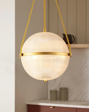 Modern gold globe pendant light with a textured glass shade hanging in a contemporary kitchen.