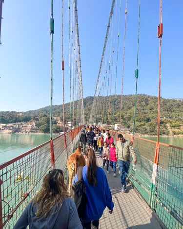 View of the iconic suspension bridge over the sacred Ganges River in Rishikesh, India, surrounded by lush greenery and hills.