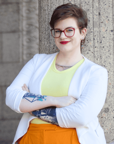 a photo of Swana Schuchmann with short hair, a white blazer and glasses, smiling