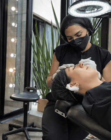 Esteticista profesional realizando microblading de cejas en un salón de belleza.