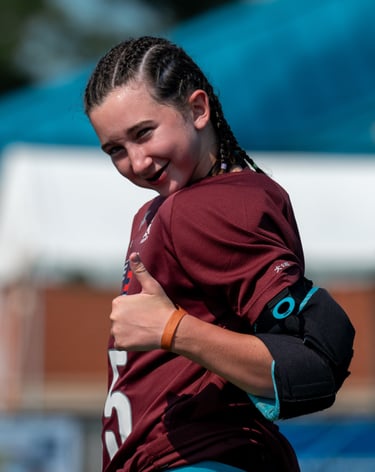 a field hockey goalie in a maroon jersey shirt is smiling and giving a thumbs up
