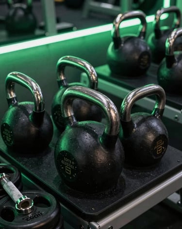 A close-up, sharp architectural shot of high-end gym equipment including heavy kettlebells and stainless steel weights. The lighting is low and moody with electric green neon glows reflecting off black surfaces. Premium fitness movement atmosphere.