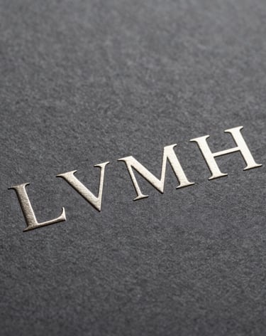 Macro shot of premium branding materials for LVMH, embossed silver logo on heavy textured dark gray paper, elegant minimalist design, soft directional lighting, Southern European style.