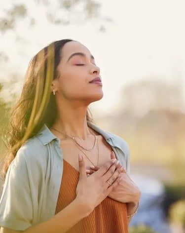Une femme respire profondément en se tenant debout à l'extérieur, savourant un moment de sérénité et de connexion.