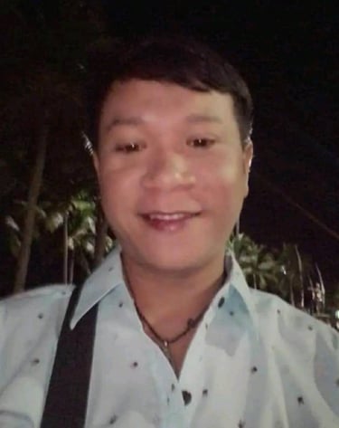 Man smiling outdoors at night in Pattaya, Thailand, wearing a light shirt and shoulder bag.