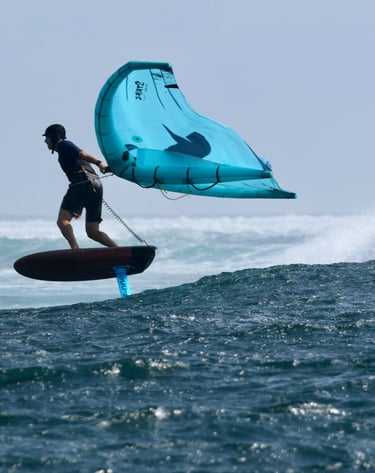 a man is holding a wing on a  foil board in the water, over a wave