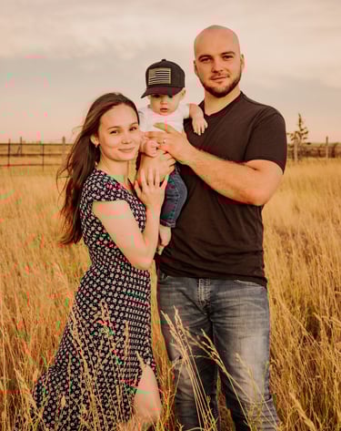 a man and woman standing in a field holding a baby