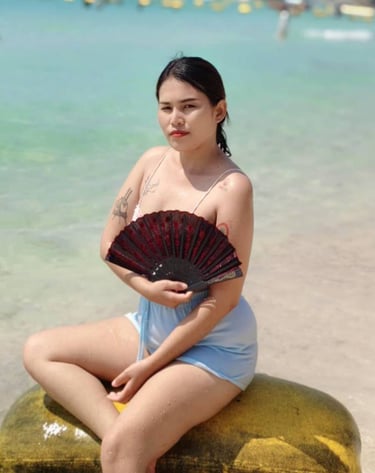Lady sitting on a float at the beach and holding a fan in her hand