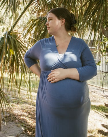 a pregnant woman in a blue dress standing in front of a palm tree