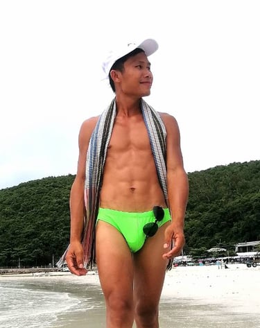 Man walking along Pattaya Beach wearing green swimming trunks.