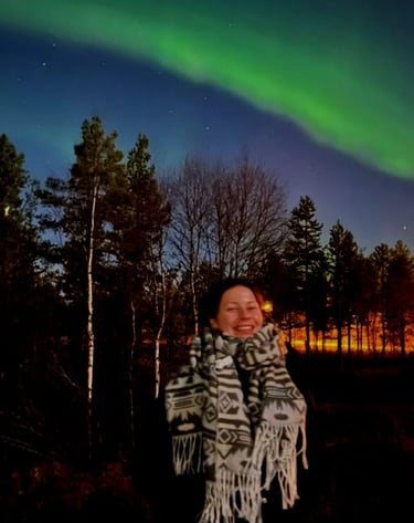 a woman standing under the northern lights with a smile