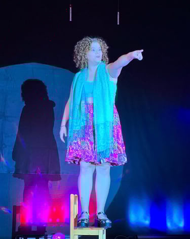 ein lockiges Mädchen auf einem Stuhl stehend im Spotlight auf der Bühne